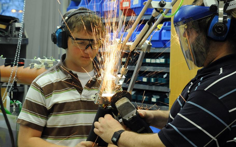 Sparks fly as RoboWarrior club adviser Frank Pendzich uses a little low-tech to grind off a pair of screws from the arm of the club's robot, as Tim Kanser holds the arm steady. The Wiesbaden High School robotics club members put the final touches on their robot before shipping it off to the FIRST Robotics Competition in Las Vegas.